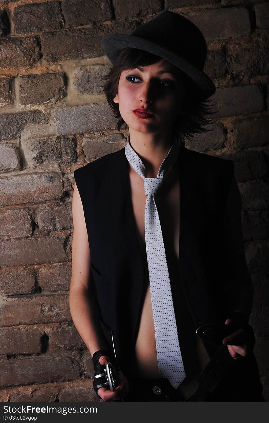 Girl in a tie and hat on near a brick wall. Girl in a tie and hat on near a brick wall