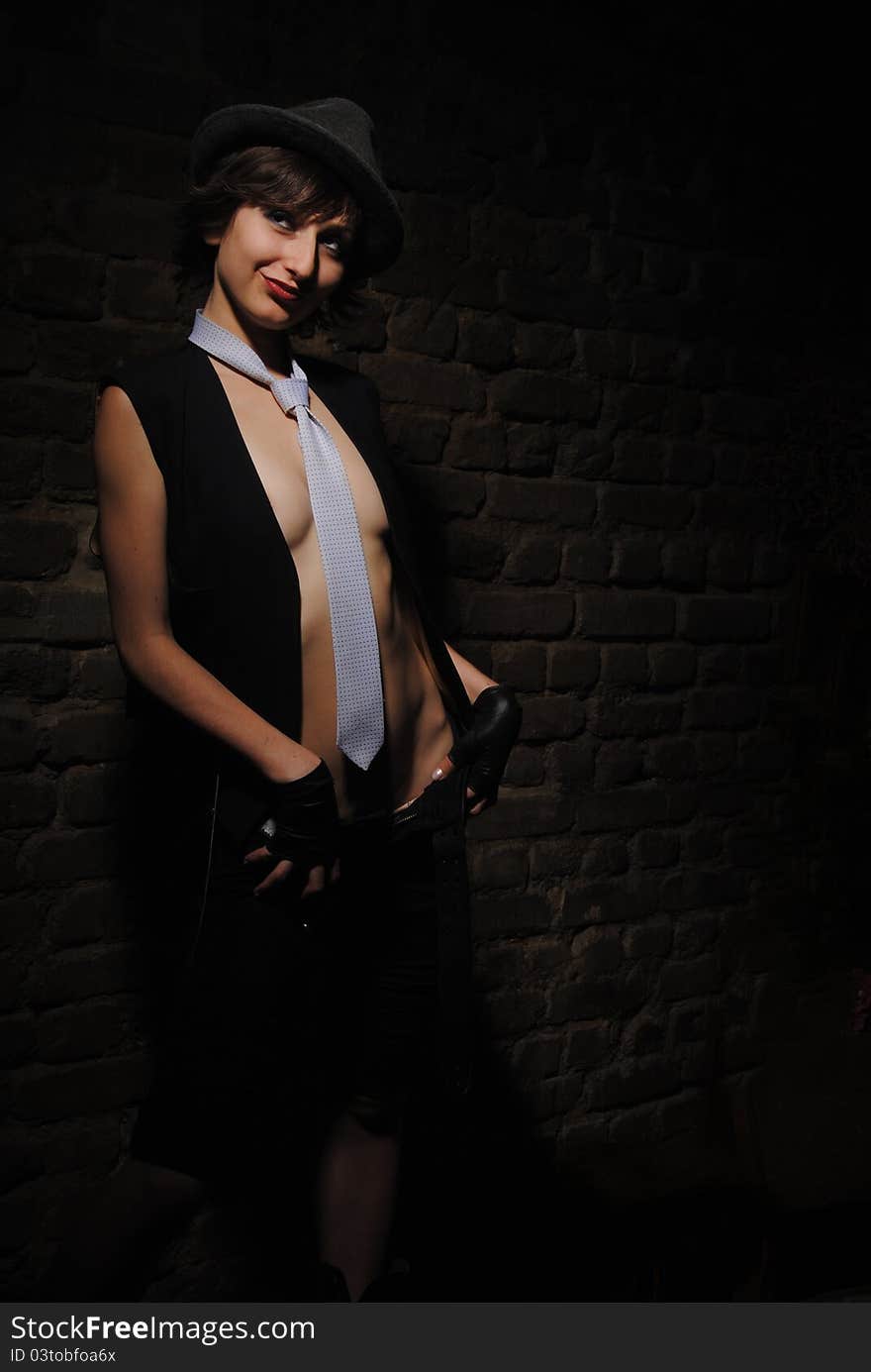 Girl in a tie and hat on near a brick wall. Girl in a tie and hat on near a brick wall