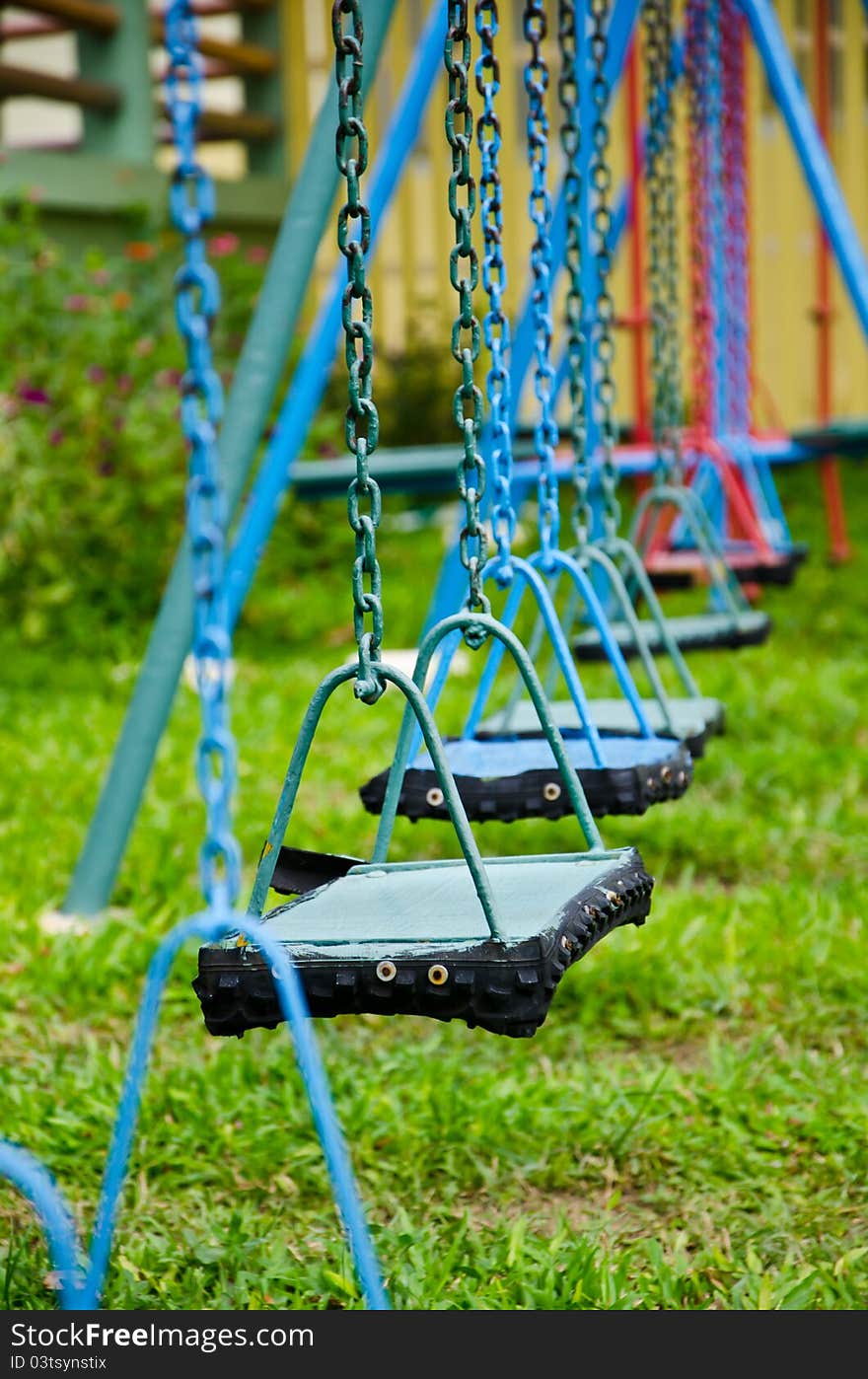 Blue and red swings hanging in the green park