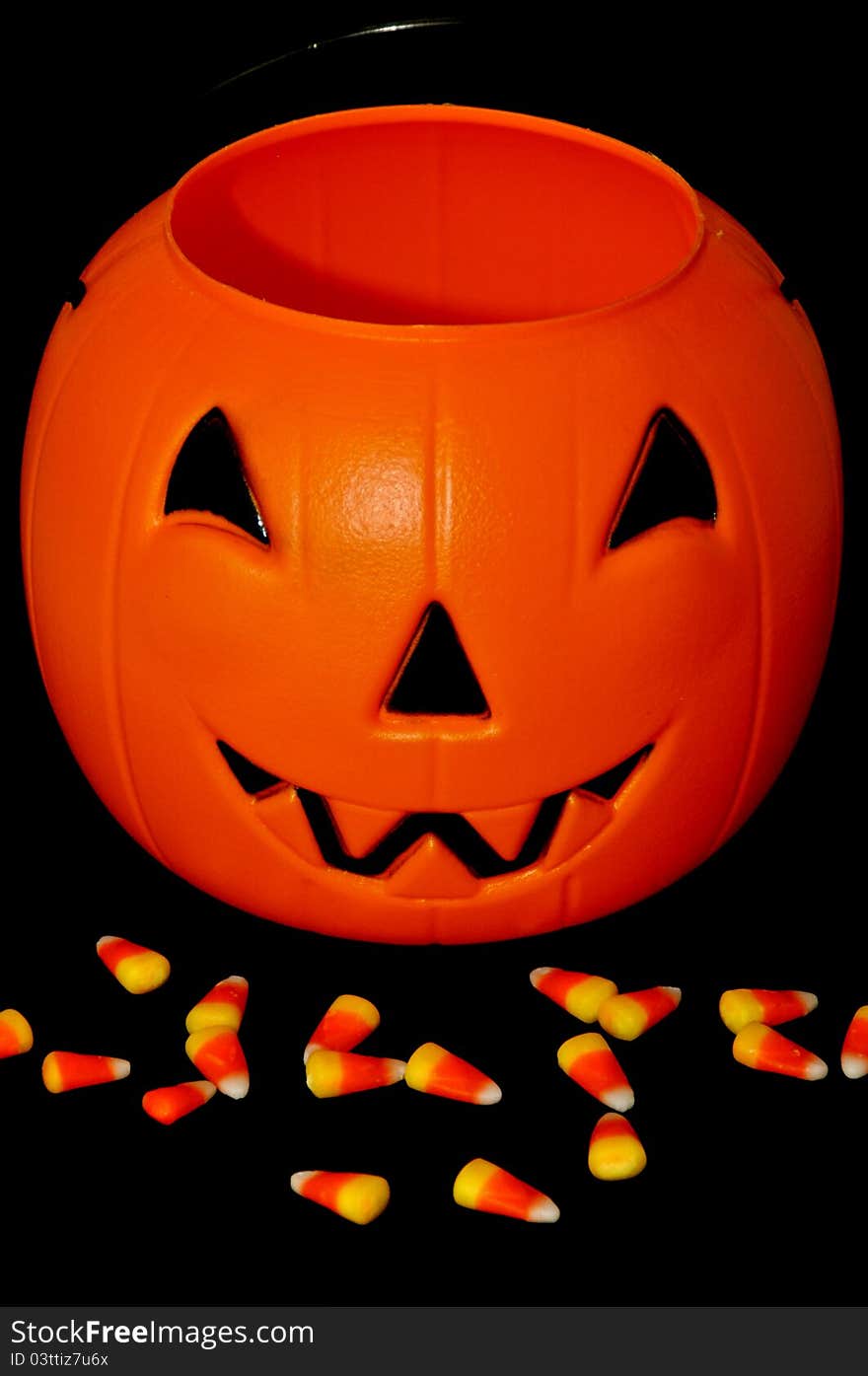 Plastic pumpkin with candy corn in front of it against black background. Plastic pumpkin with candy corn in front of it against black background