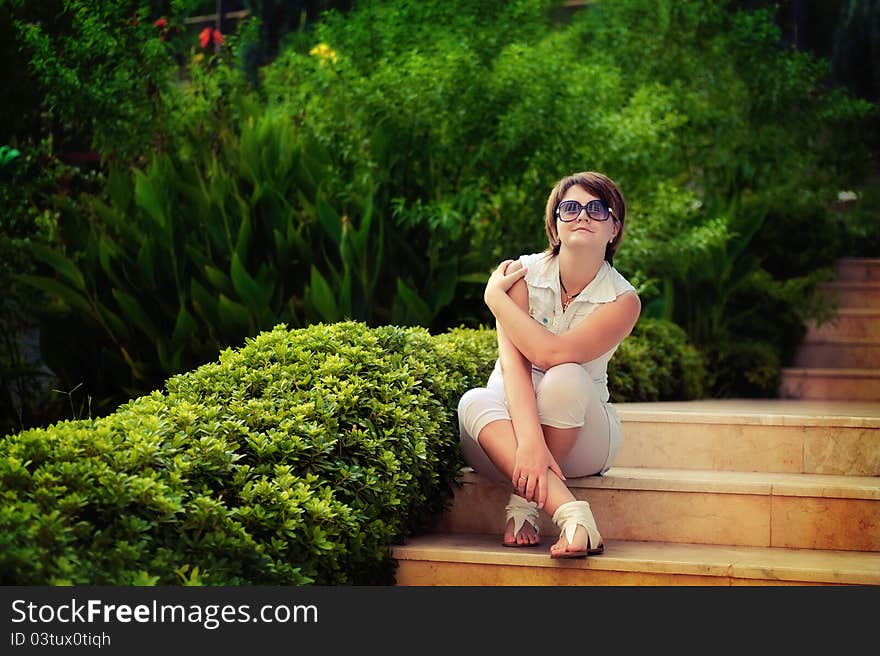 The girl in park in the summer on avenue between bushes of greens wearing spectacles