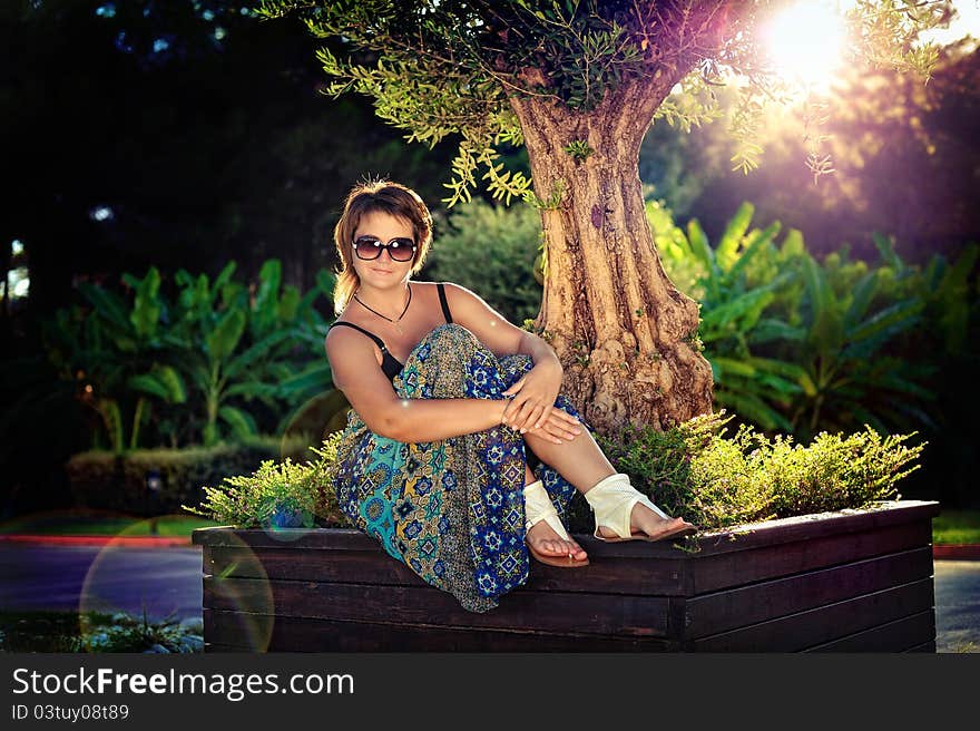 The girl in park in the summer on avenue between bushes of greens wearing spectacles