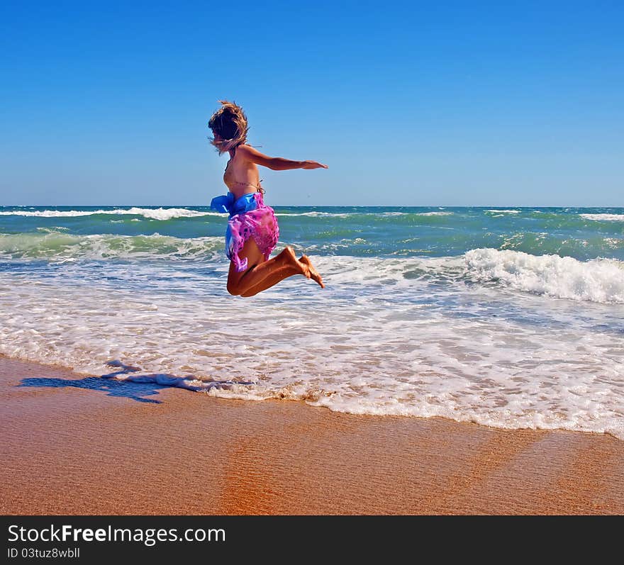 Girl in pareo jumping on the coastline