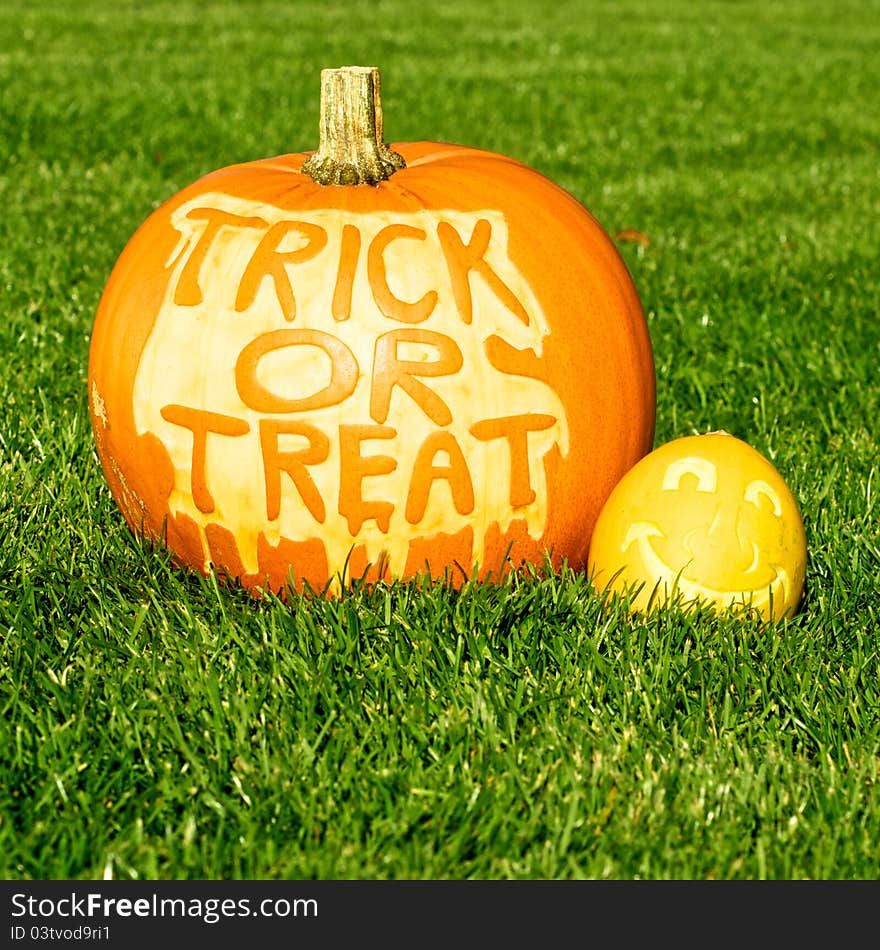 Picture o one big and one small pumpkin, standing on a lawn. Small pumpkin has a face cut in the surface, and the big has Trick Or treat cut in the surface. Picture o one big and one small pumpkin, standing on a lawn. Small pumpkin has a face cut in the surface, and the big has Trick Or treat cut in the surface