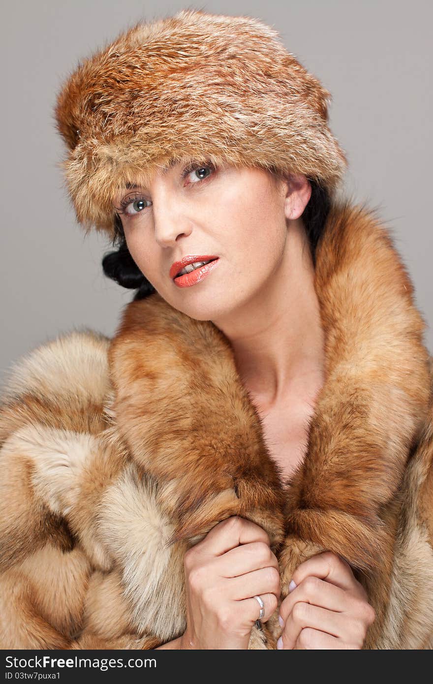 Mature seducing brunette in fox fur  and fox hat on gray background. Mature seducing brunette in fox fur  and fox hat on gray background