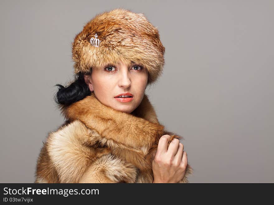 Mature seducing brunette in fox fur  and fox hat on gray background. Intents look. Mature seducing brunette in fox fur  and fox hat on gray background. Intents look