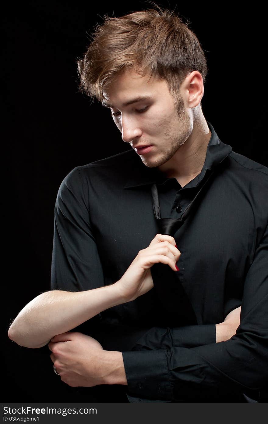 Woman slowly undressing man in a tie and black shirt. Black background. Woman slowly undressing man in a tie and black shirt. Black background