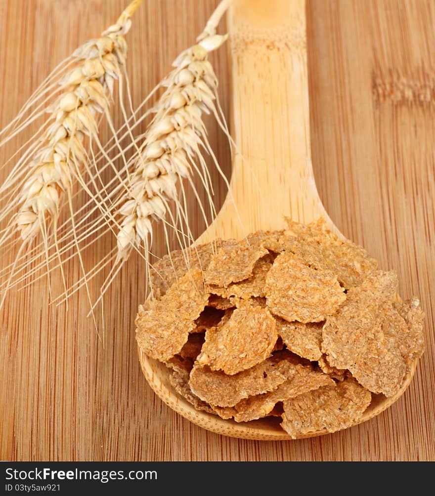 Two wheat heads next to a wooden spoon of wheat flakes. Two wheat heads next to a wooden spoon of wheat flakes
