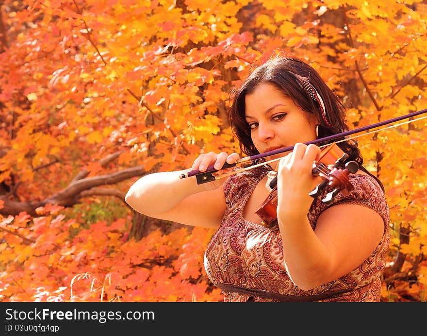 Pretty woman playing her violin with an autumn color backdrop. Pretty woman playing her violin with an autumn color backdrop.