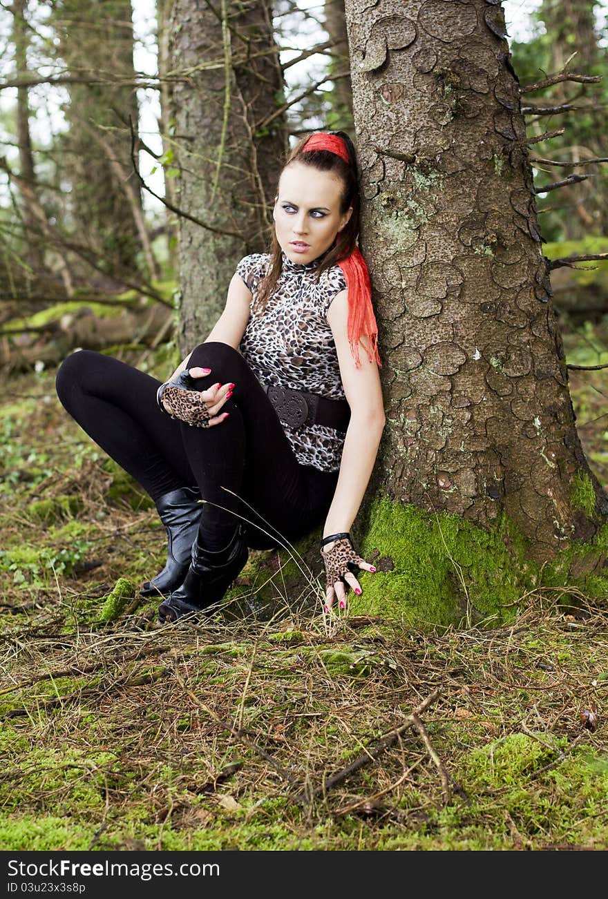 Young woman crouching beside a mossy tree in the forest. Young woman crouching beside a mossy tree in the forest