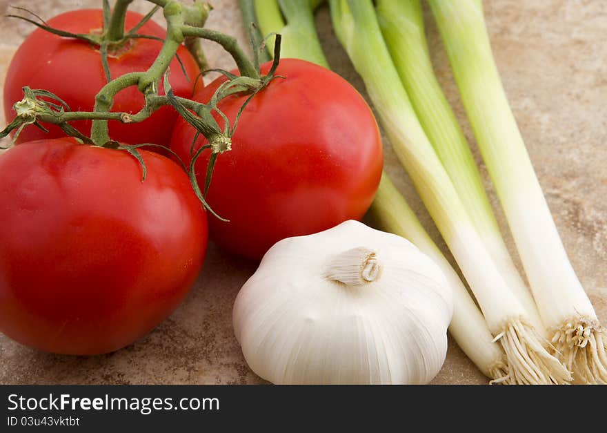 Vine ripe tomatoes, garlic and spring green onions photographed on kitchen counter surface. Vine ripe tomatoes, garlic and spring green onions photographed on kitchen counter surface