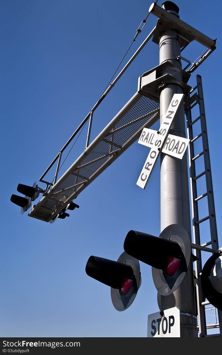 Overhead railroad crossing flashing under blue sky
