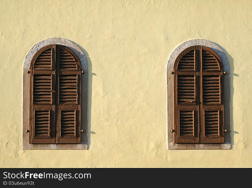 Two old brown wooden windows of the yellow wall