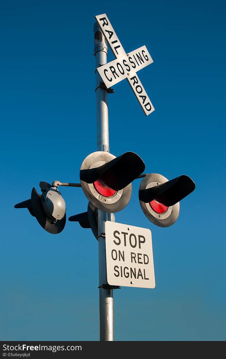 Overhead railroad crossing flashing under blue sky