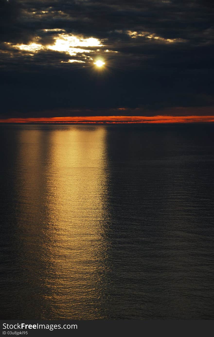 The path of light stretches across the tranquil sea. The North sky is covered with clouds but the sun struggles through the overcast. The picture is made at the midnight during the polar day. The path of light stretches across the tranquil sea. The North sky is covered with clouds but the sun struggles through the overcast. The picture is made at the midnight during the polar day.