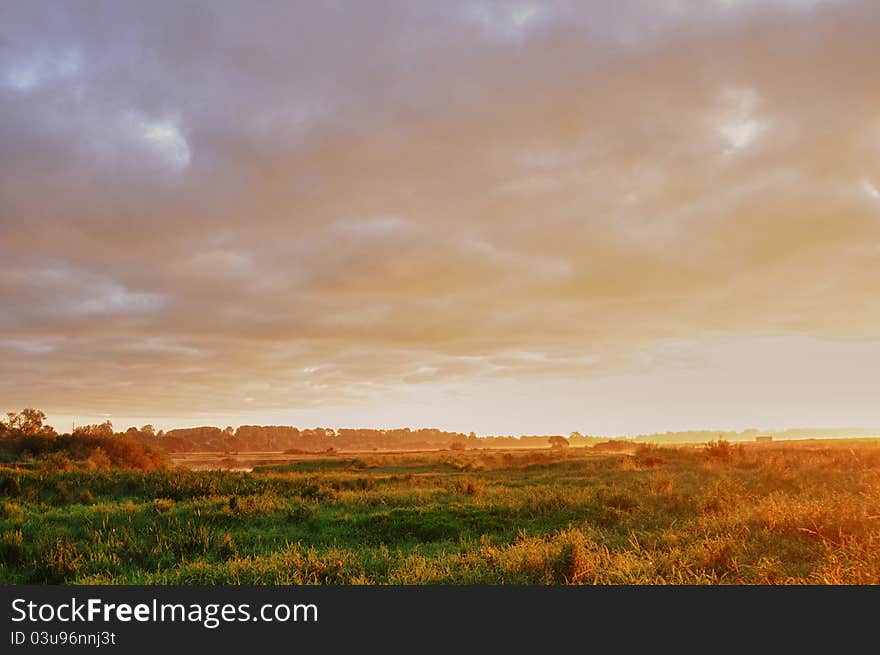 The rays of a getting up sun slide on a green meadow and light up sky. The rays of a getting up sun slide on a green meadow and light up sky