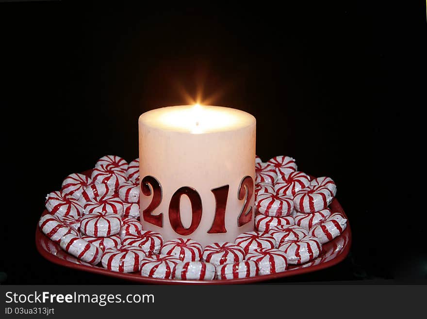 A 2012 Candle lit for the new year with peppermint candy placed around it on a red plate. A 2012 Candle lit for the new year with peppermint candy placed around it on a red plate.