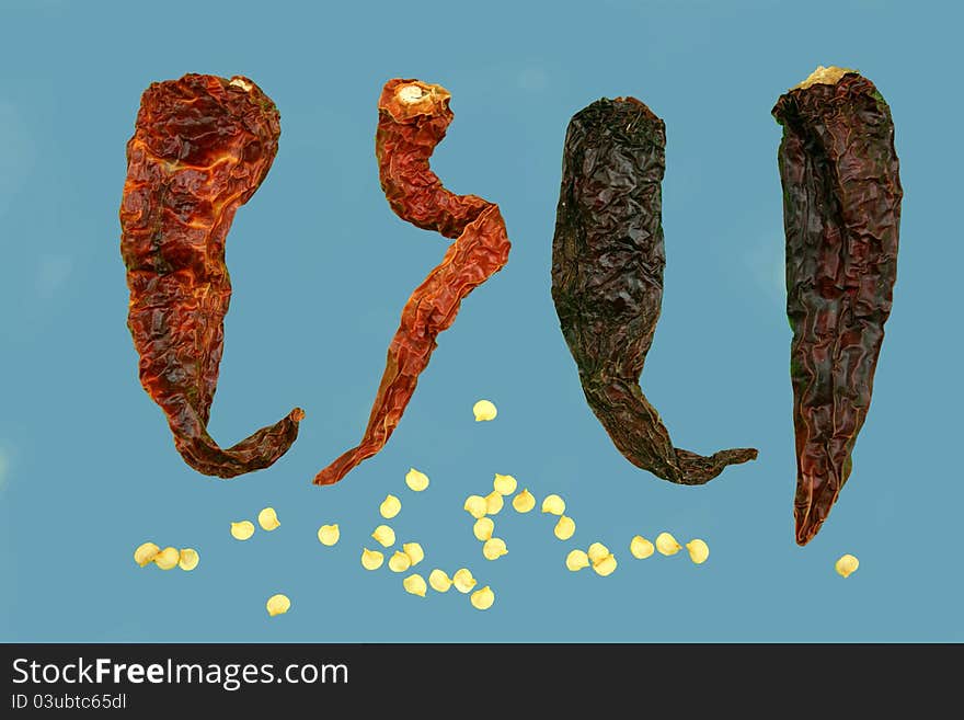 Four isolated dried red Kashmiri chillies with scattered isolated and grouped chilli seeds. Four isolated dried red Kashmiri chillies with scattered isolated and grouped chilli seeds.