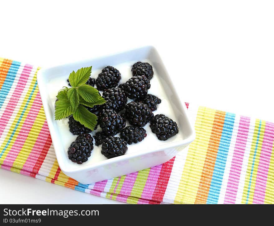 Blackberries on yogurt in a white, square, porcelain dish on a striped cloth. on a white background.