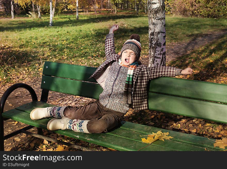 Boy stretching and yawning on park bench in autumn. Boy stretching and yawning on park bench in autumn.