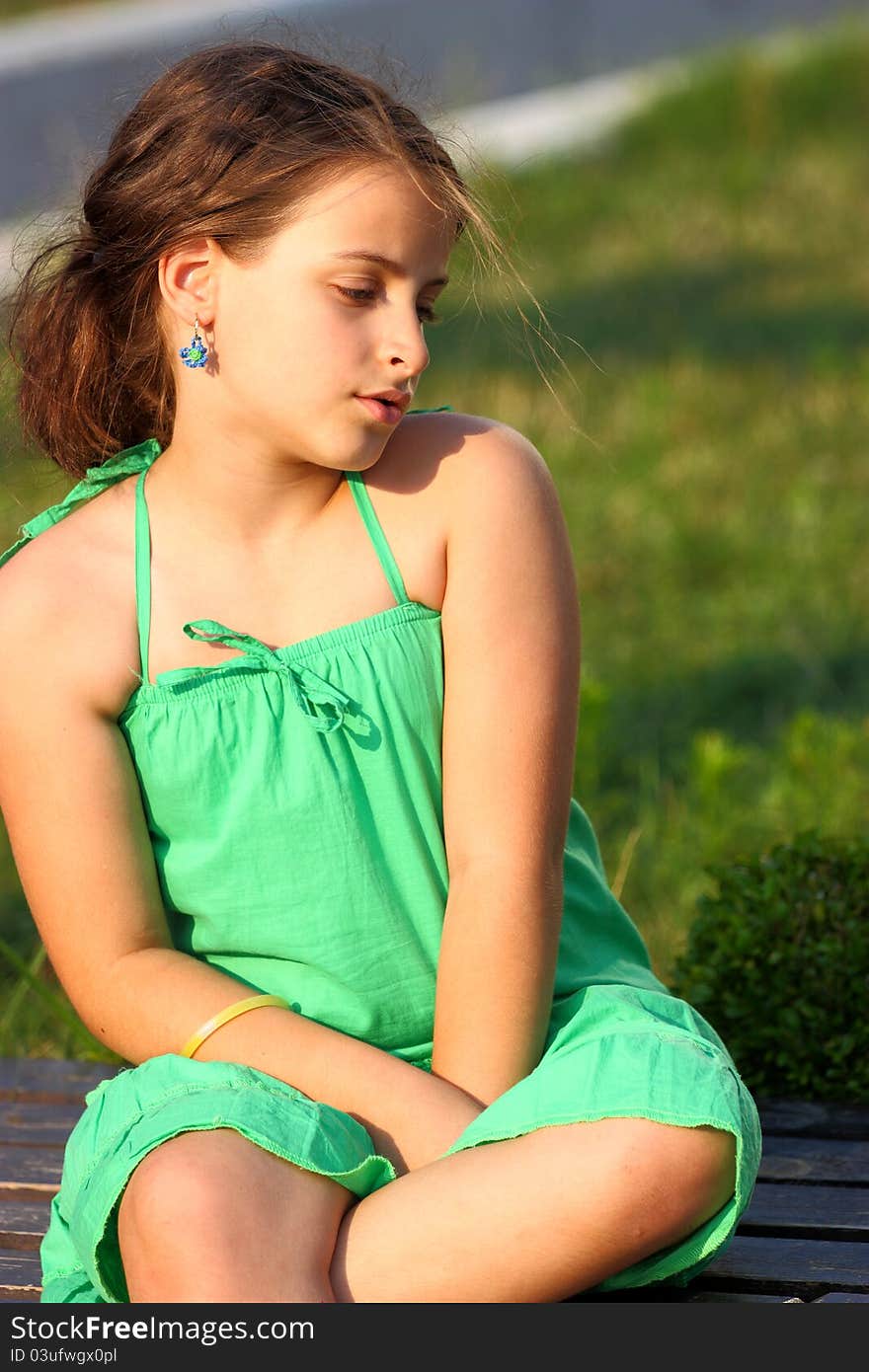 A girl sitting on a wooden bench outdoor in a green park. A girl sitting on a wooden bench outdoor in a green park