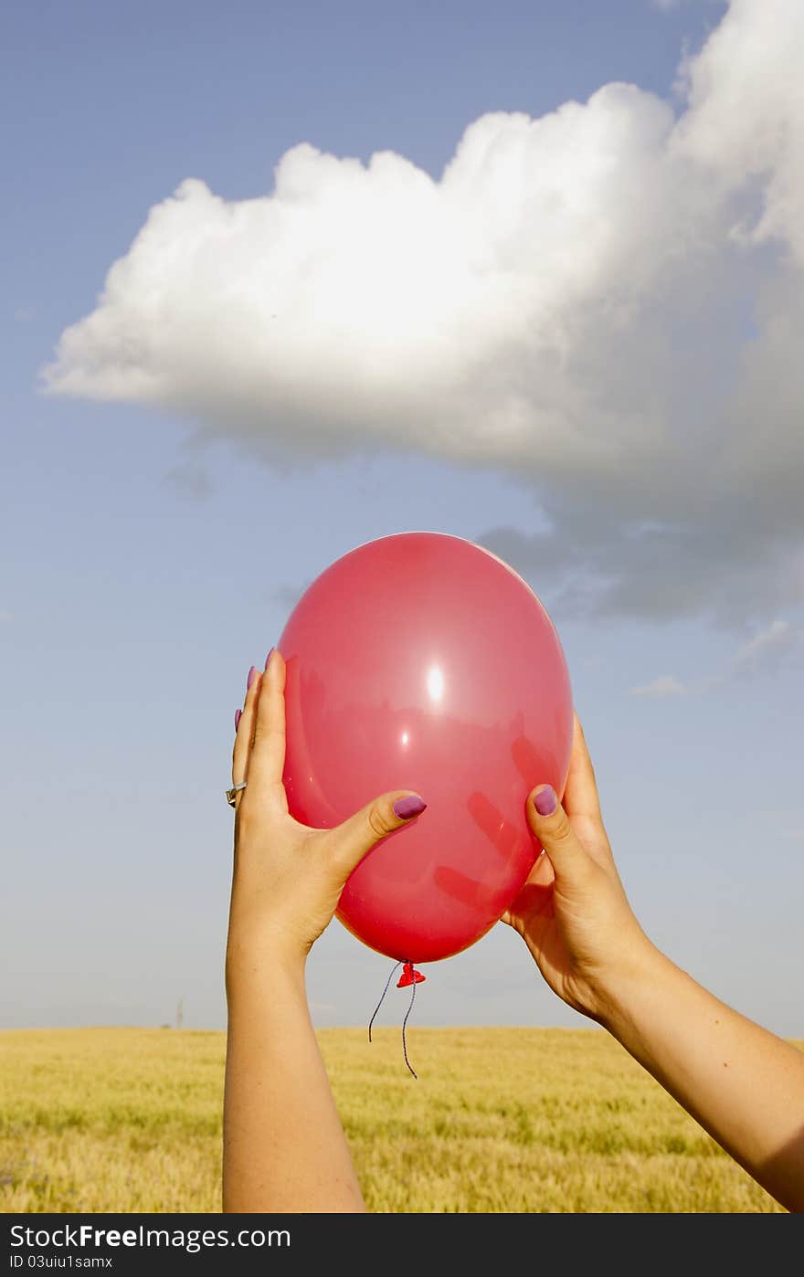 Woman hands holding red balloon. Agricultural field and sky with clouds in background. Woman hands holding red balloon. Agricultural field and sky with clouds in background.