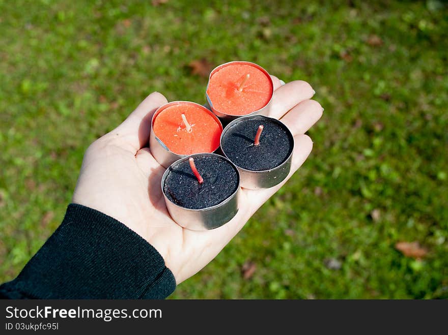 Hand holding black and orange tealights, outside. Hand holding black and orange tealights, outside