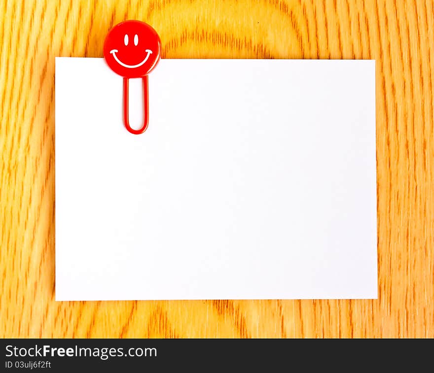 Close up of a red paper clip and white paper on wood table