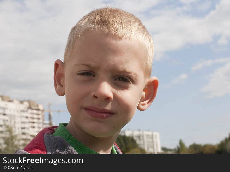 The boy of five years against the sky and buildings poses for a portrait. The boy of five years against the sky and buildings poses for a portrait