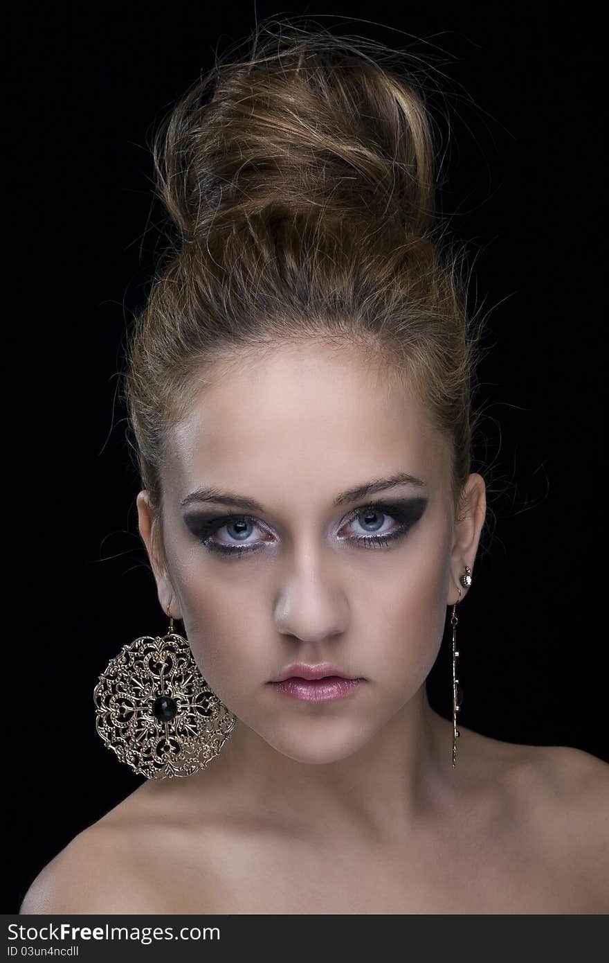 Young woman with blue eyes, bare shoulders, earrings and black background. Young woman with blue eyes, bare shoulders, earrings and black background