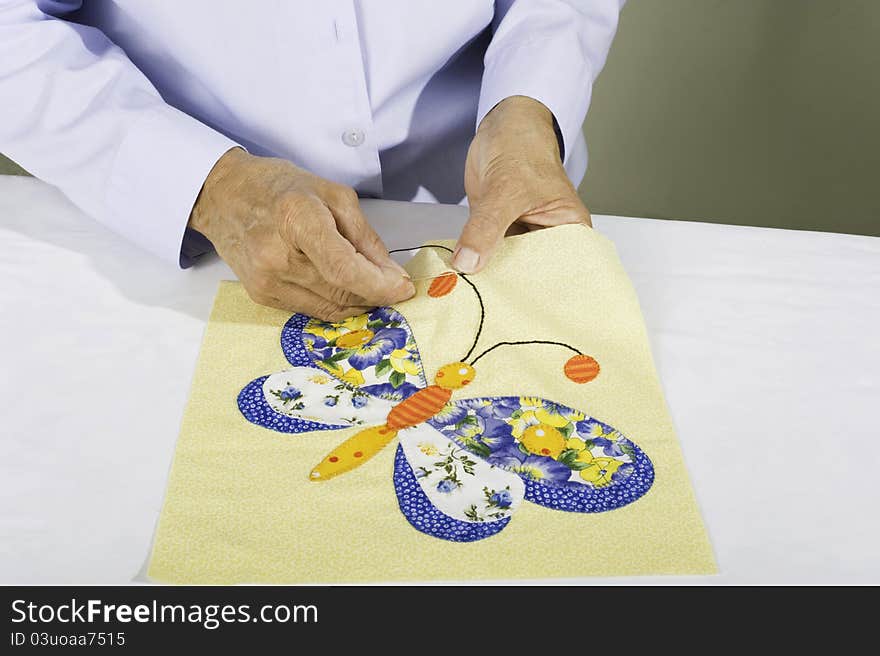 A woman stitches black thread to a quilt panel of a butterfly. A woman stitches black thread to a quilt panel of a butterfly.