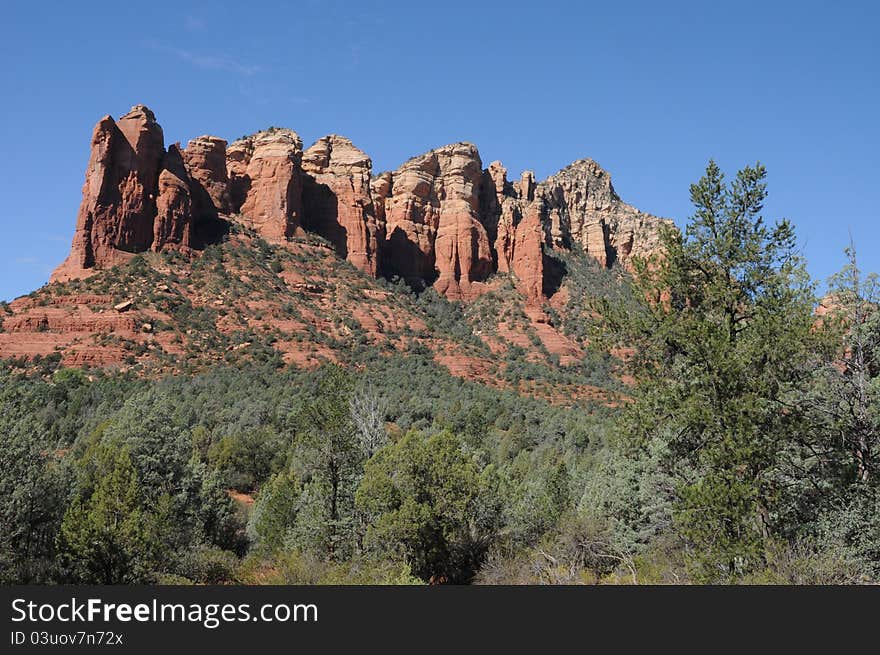 Looking at a rock ledge in Sedonna Arizona, red rock pillars with blue sky, and low grass and greens near the base