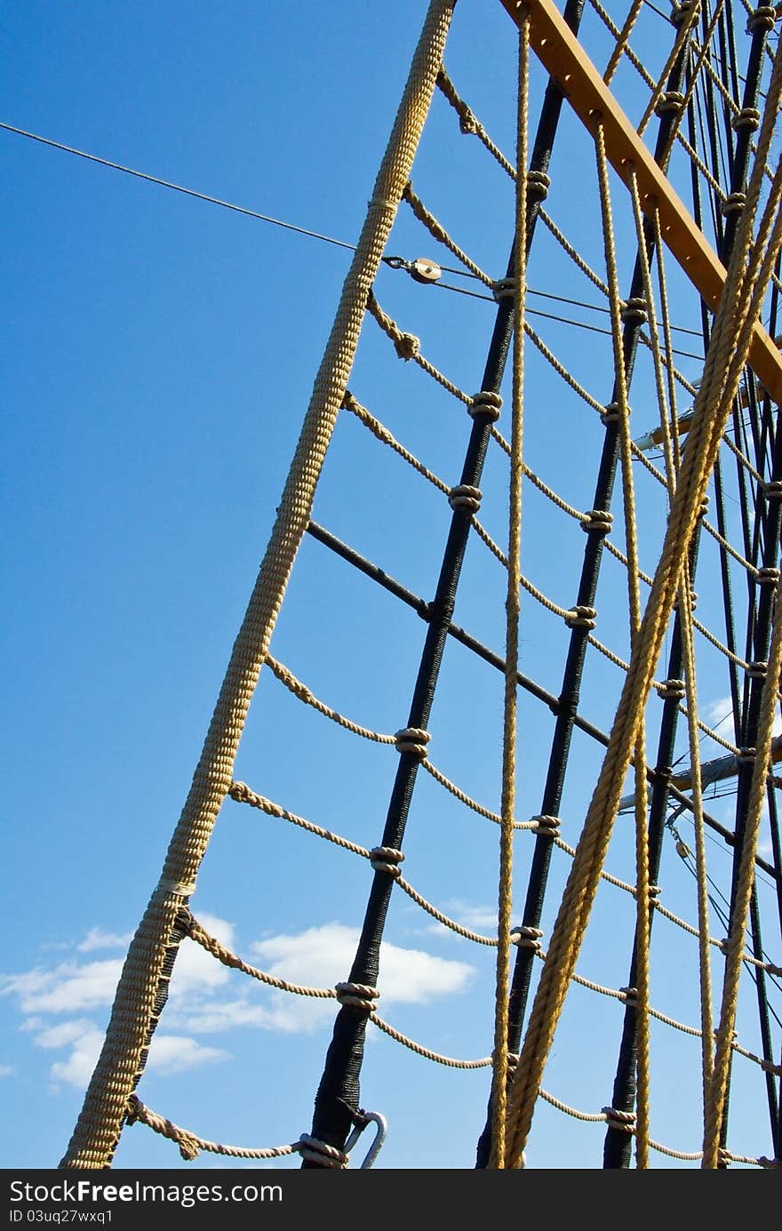 Marine rope ladder at pirate ship. Sea hemp ropes on the old nautical vessel. Ladder upstairs on the mast. Sailing ship detail at blue sky background.