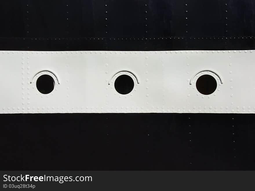 Three porthole window on a ship's hull. Black and white stripes with a round windows on board the ship with rivets. Three porthole window on a ship's hull. Black and white stripes with a round windows on board the ship with rivets.