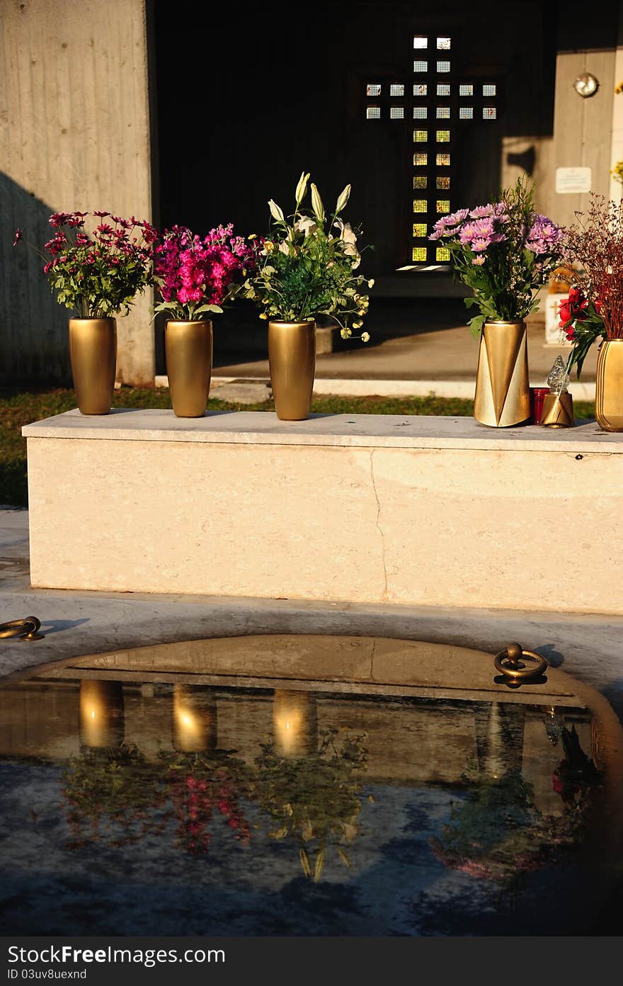 Grave with flowers in the cemetery with cross on the bottom and reflection in the water