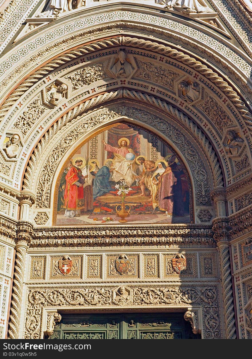 Details of the facade around the door of the Basilica di Santa Maria del Fiore - Florence Cathedral. Marble details and neo-gothic style architecture with coats of arms surround the central lunette mosaic. Details of the facade around the door of the Basilica di Santa Maria del Fiore - Florence Cathedral. Marble details and neo-gothic style architecture with coats of arms surround the central lunette mosaic