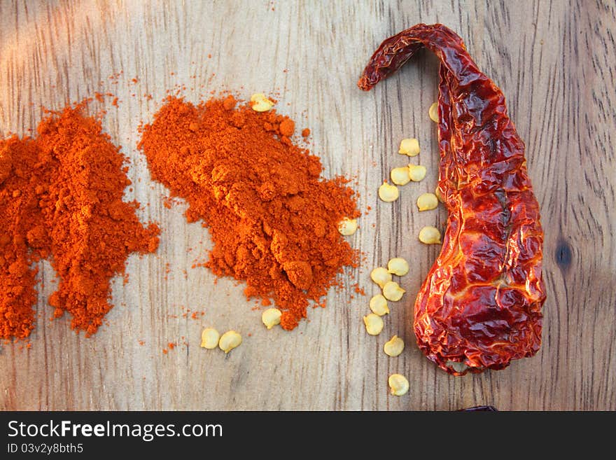 A single dried red chilli pictured next to some chilli seeds and some ground red chilli powder.