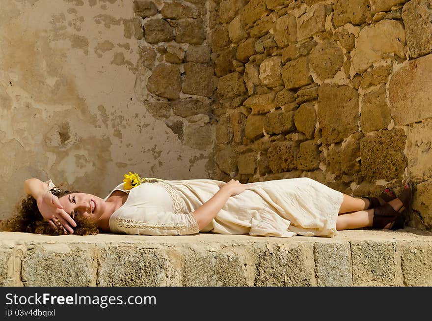 Beautiful Young attractive girl model lie down on wall and posing for a portrait against an outdoor rock wall. Beautiful Young attractive girl model lie down on wall and posing for a portrait against an outdoor rock wall.