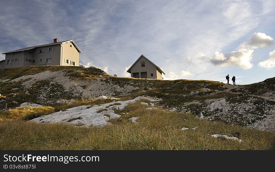 Alpine lodge in the middle of Slovenian Alps - scenery with sunset and two hikers at Pogacnikov dom