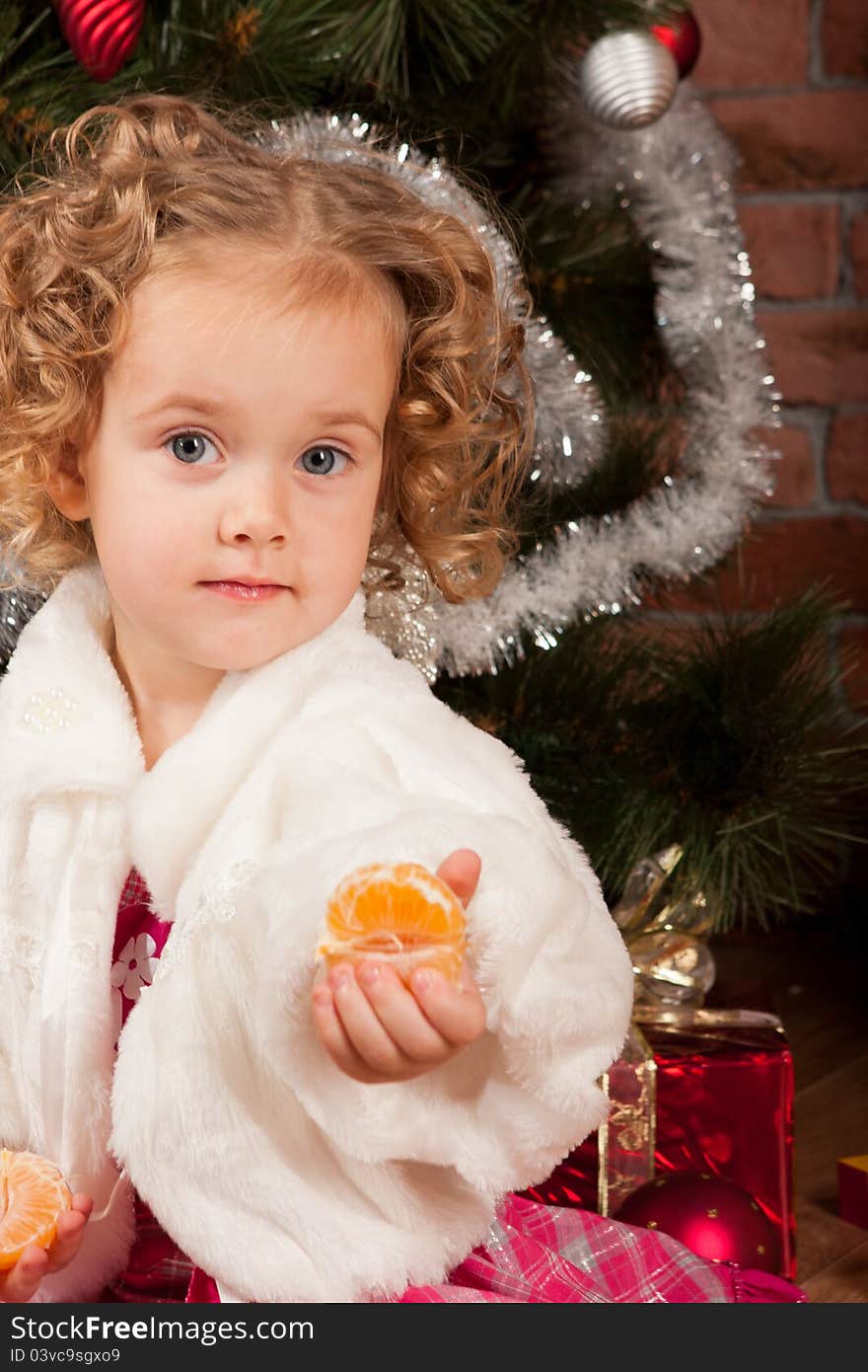 Preaty little girl eating tangerine near Christmas tree