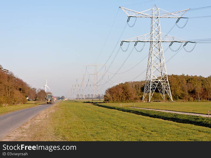 Country road with tractor and electricity pylons in Dutch farmland