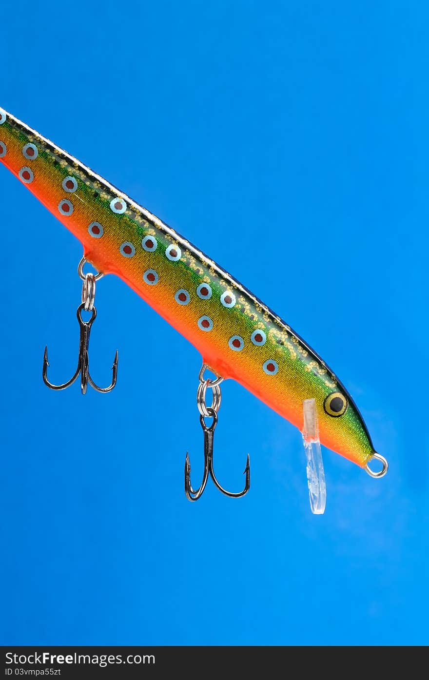A fishing bait (wobbler) with hooks on a blue background. A fishing bait (wobbler) with hooks on a blue background