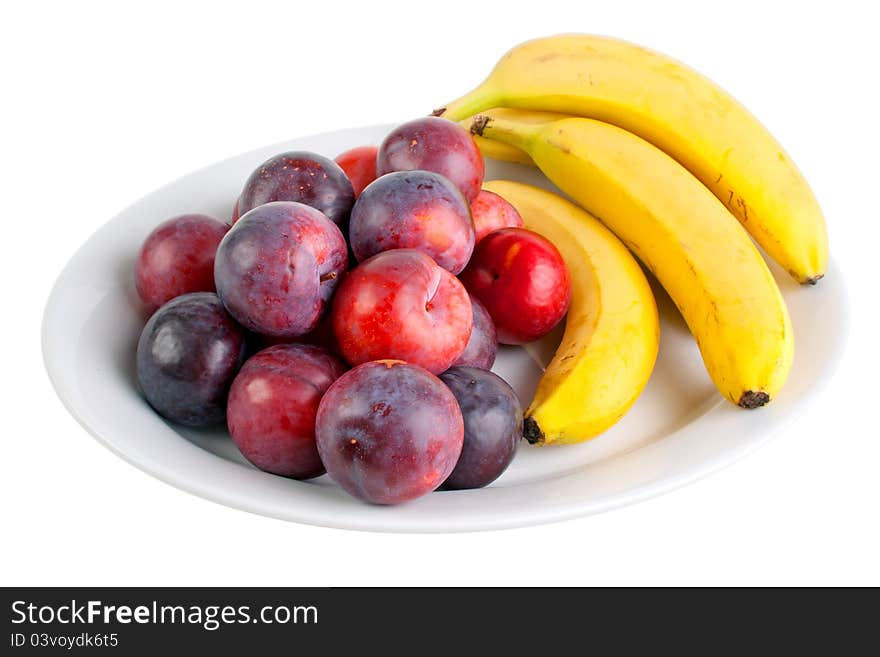 Plums and bananas on the plate, isolated on white