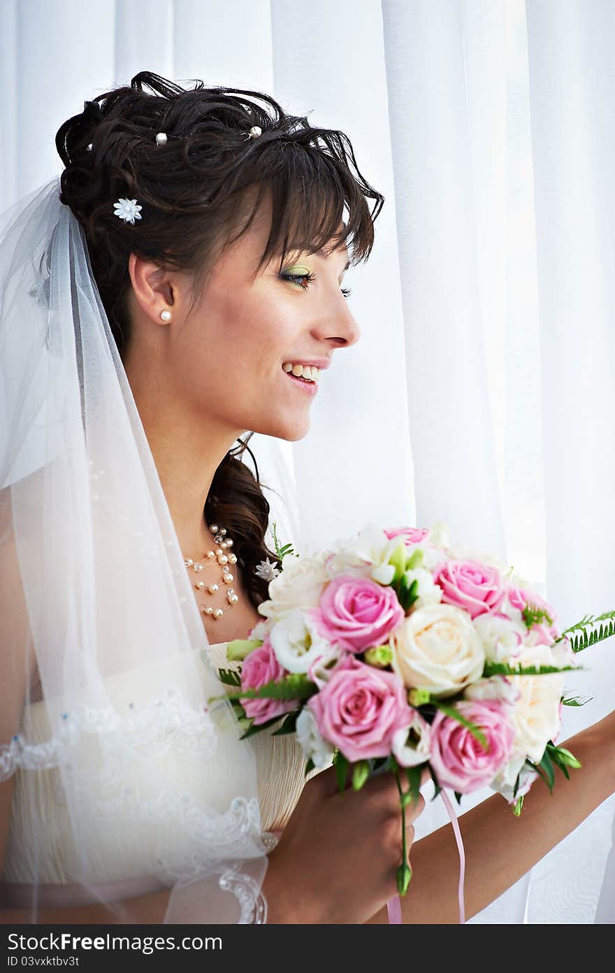 Happy bride with weding bouquet near window