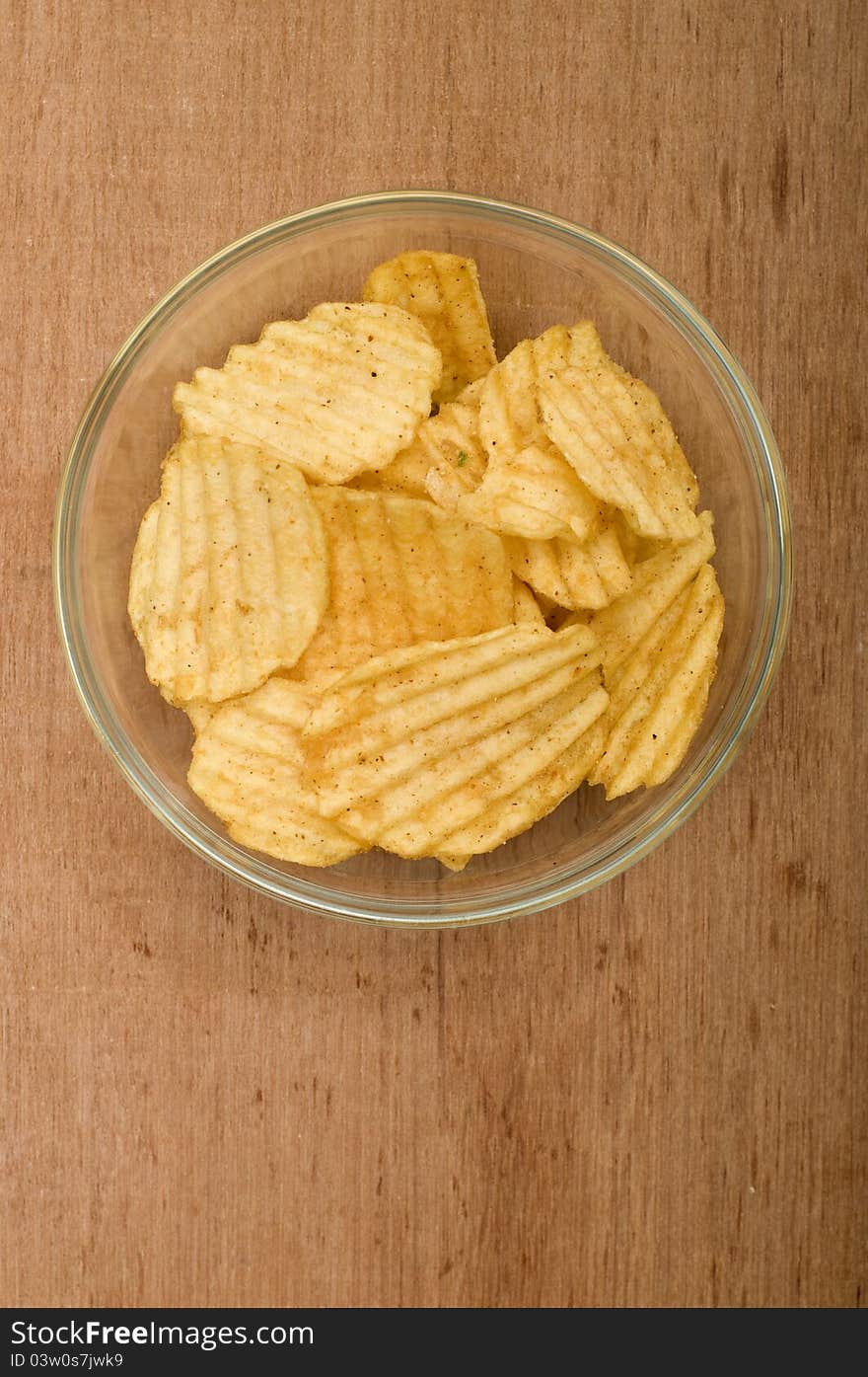 Rippled potato chips in the glass bowl over wooden background