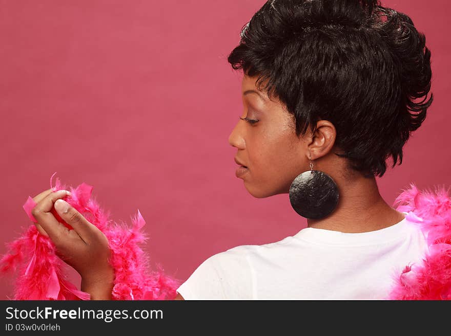 Beautiful black woman wearing a white shirt against a simple pink background with a feather boa.