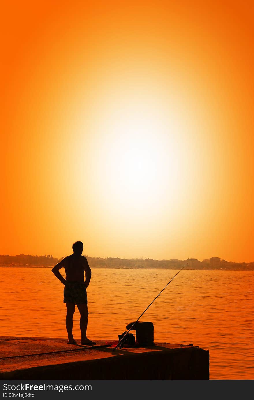 Man fishing on the pier at sunset