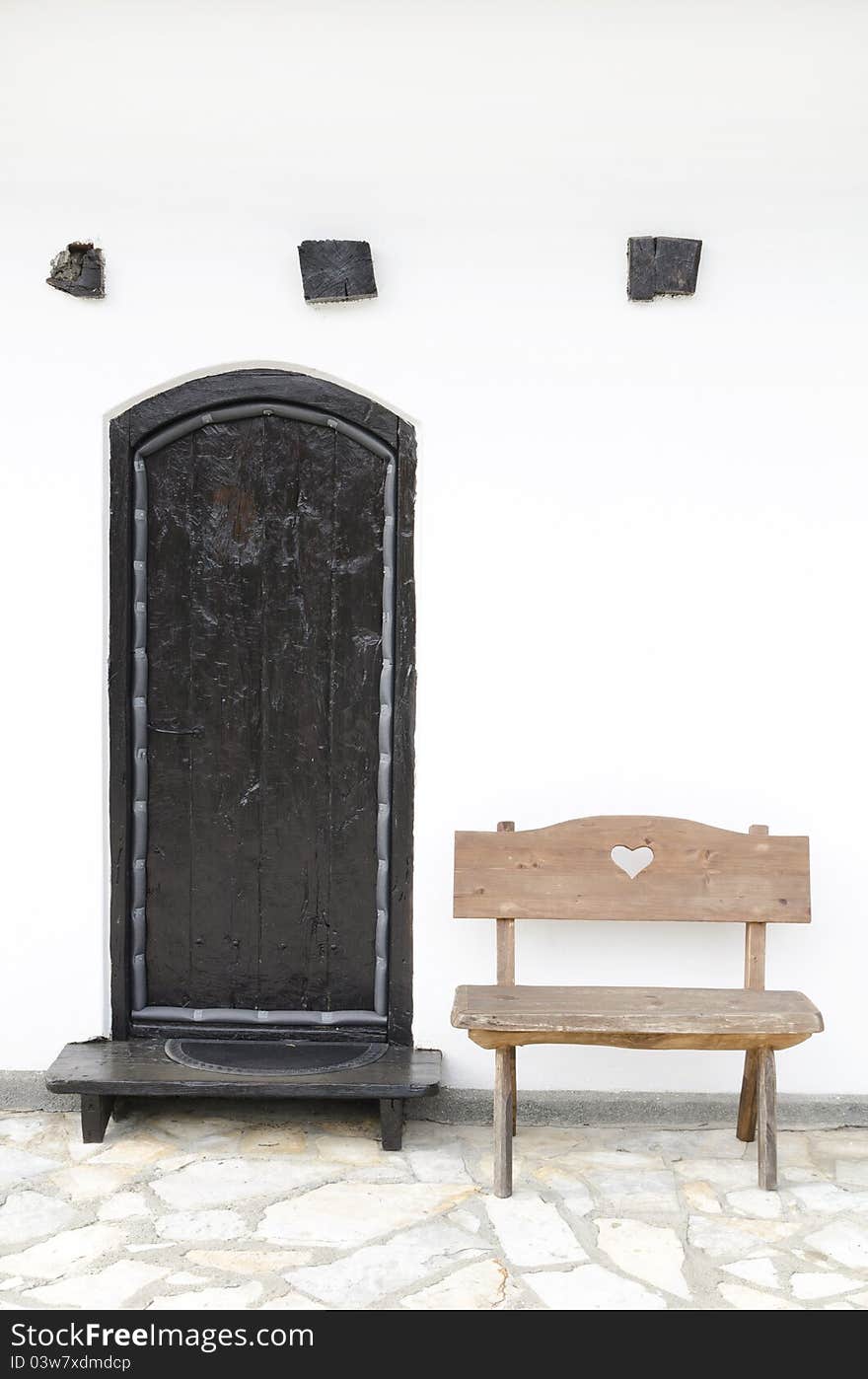 Detail of old Serbian house, wooden banch and black wooden doors against white wall. Detail of old Serbian house, wooden banch and black wooden doors against white wall