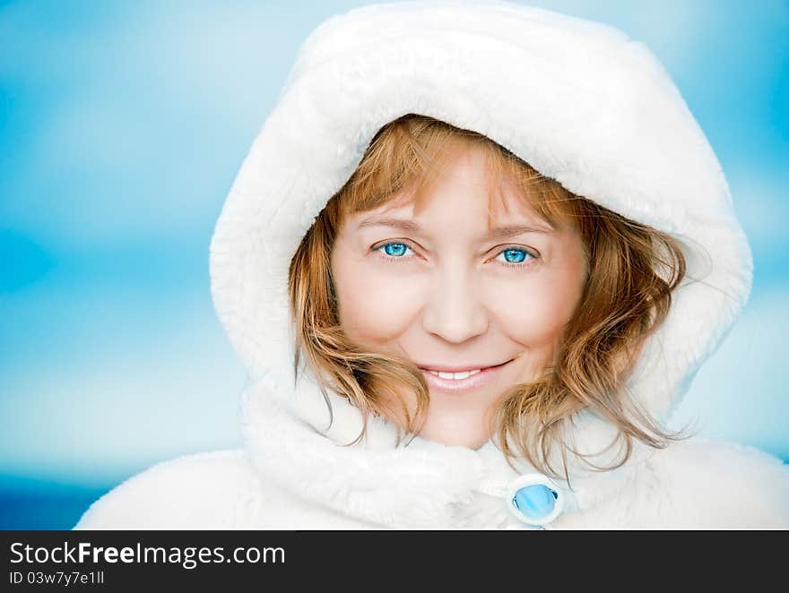 Adult woman in a white fur coat with a blue brooch against the winter sky. smiling. closeup. Adult woman in a white fur coat with a blue brooch against the winter sky. smiling. closeup.