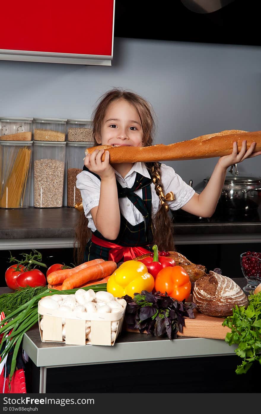 The little girl in the kitchen of chef uniforms baguette bread bites against the kitchen table with fresh produce